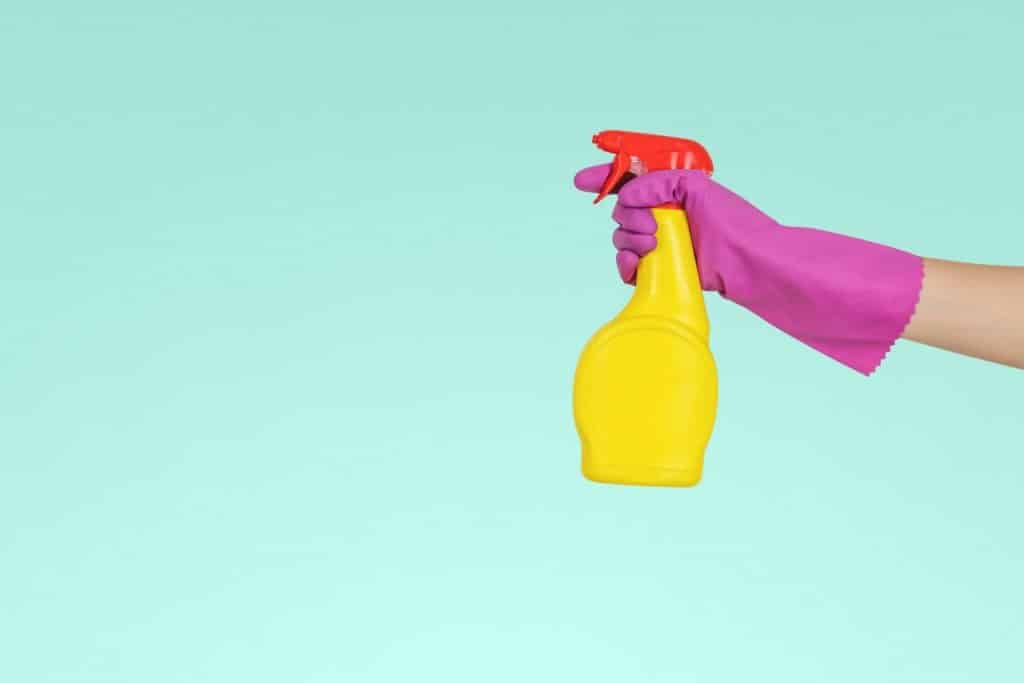 Una mano en el guante de goma con un spray de limpieza. Puede ganar dinero con el auge de Airbnb al ofrecer servicios especializados de limpieza de Airbnb.